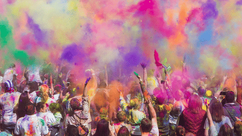 A crowd of people throwing colored powder into the air during a festival.