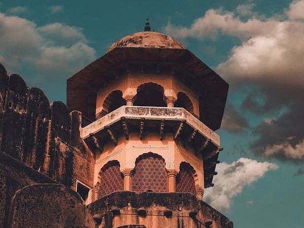 A multi-tiered tower with arched openings rises against a sky with scattered clouds.