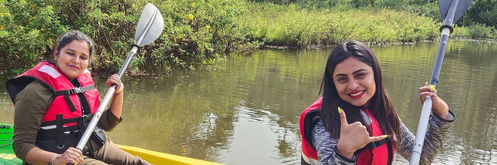 Two women in life jackets smiling while kayaking on a serene river with dense foliage in the background - Evergreen County