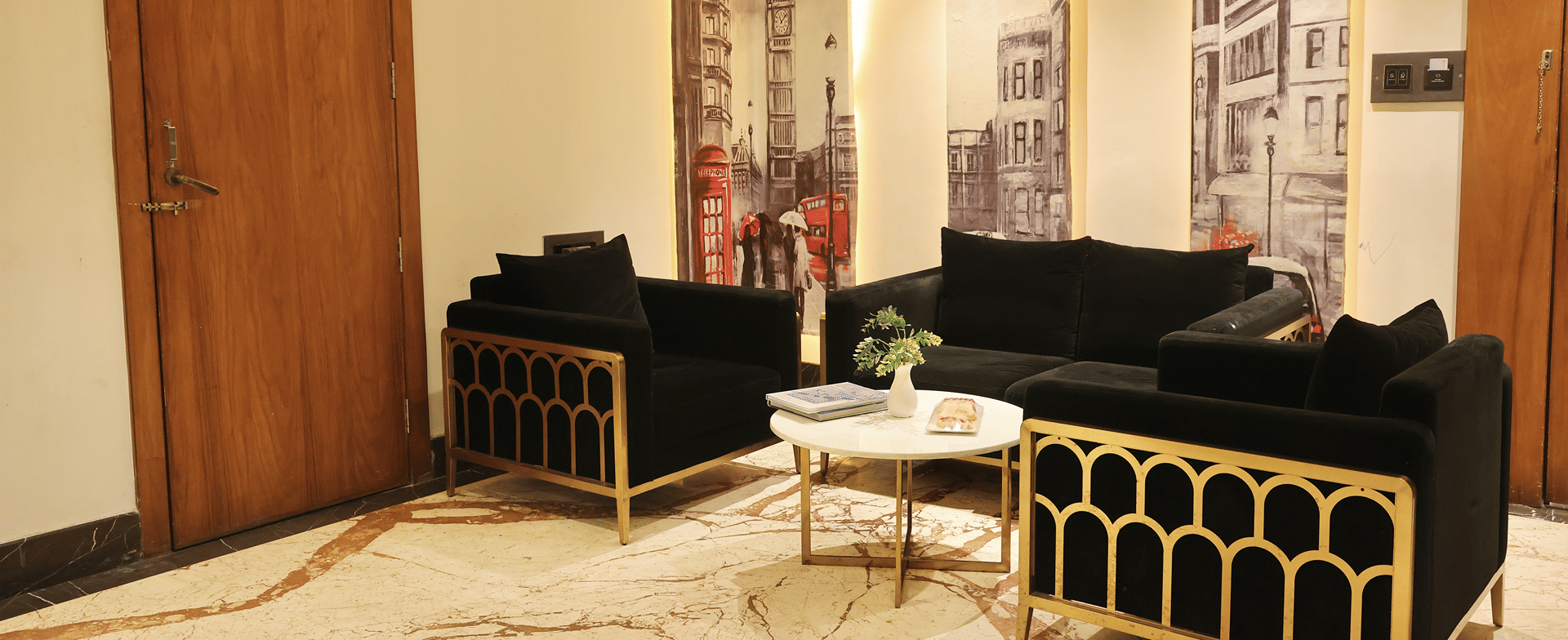 Family Room, Black velvet sofa and armchairs around a marble coffee table beneath London street murals