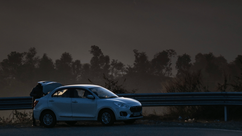 A hatchback car parked on the road side overlooking the misty mountain valleys as the sun is setting.