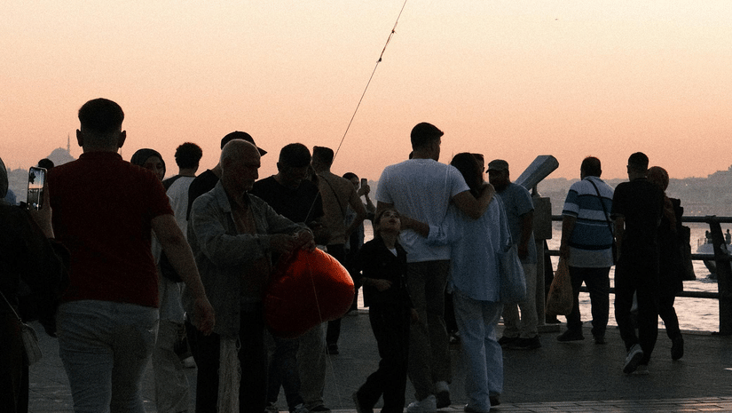 Group of people watching a street vendor selling balloons at sunset.