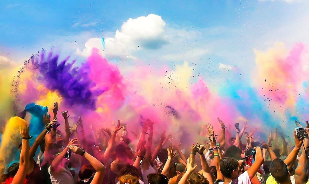Joyful group celebrating Holi with vibrant colors against a bright, clouds on the sky