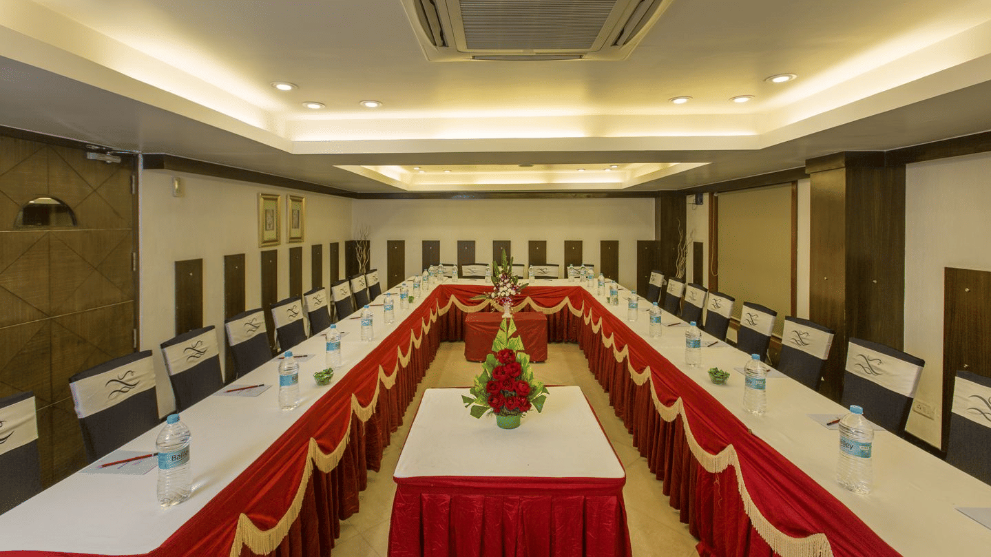A conference room with a U-shaped table arrangement, set with water bottles and flowers - The Citrine, Bangalore