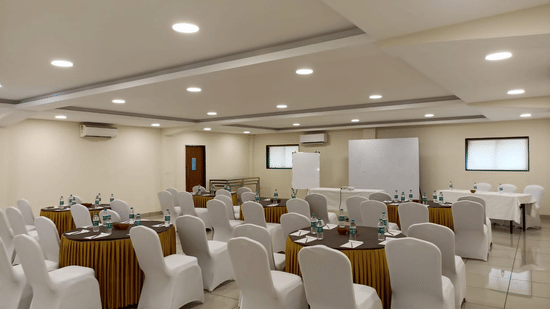 Spacious indoor conference hall setup with white chairs and tables at Nature Trails Durshet.