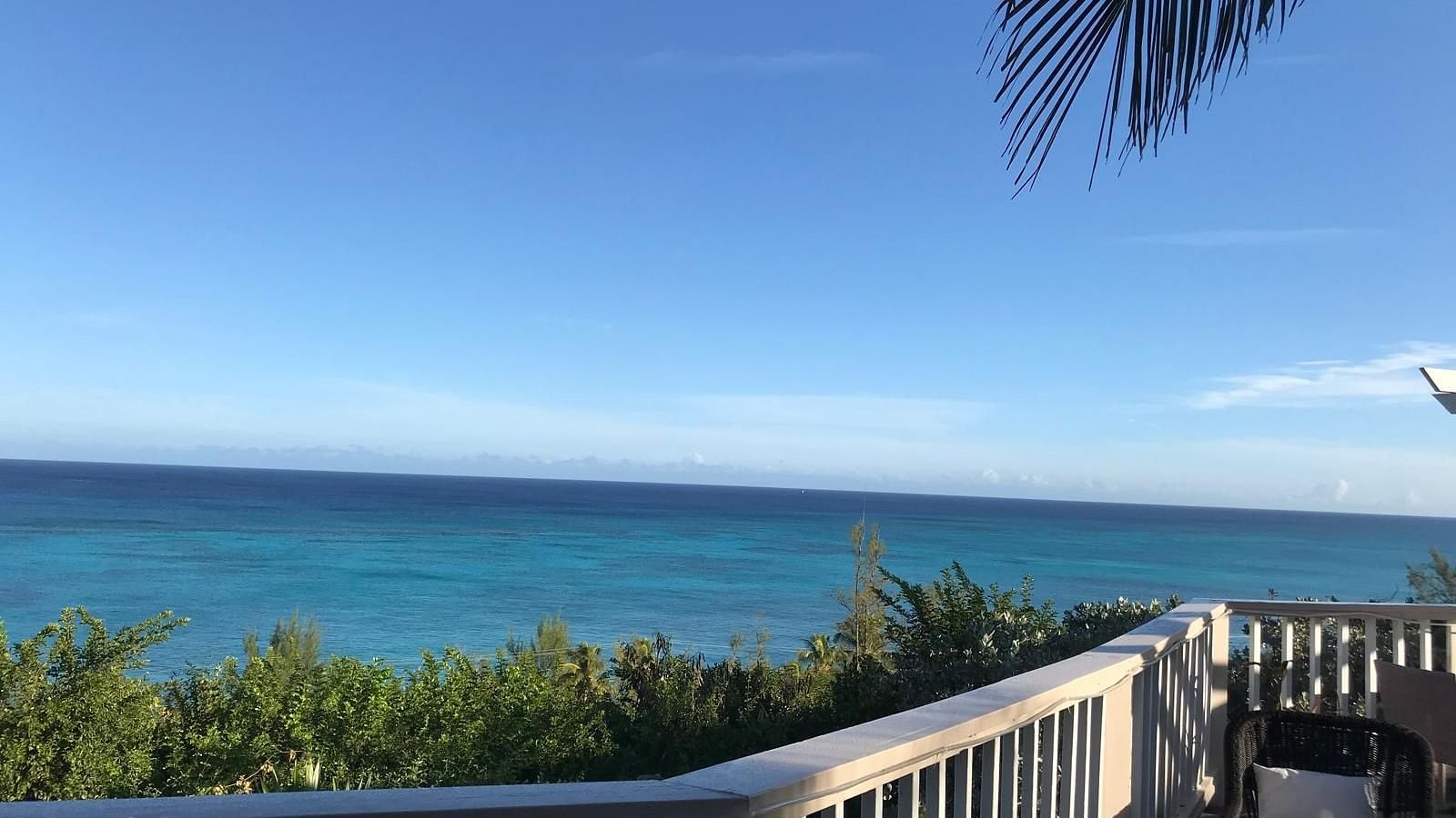 View of the ocean and trees from a deck with a chair and railing | A Stone's Throw Away