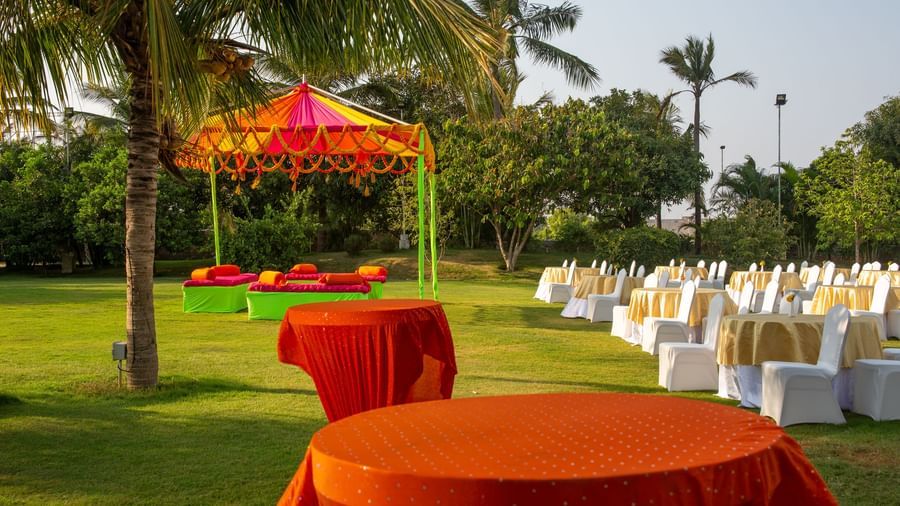 An outdoor dining area with orange-draped tables on a green lawn with palm trees and a vibrant tent | Citrus Garden | Grand Bay Resort and Spa