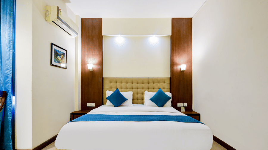 The Pamposh, New Delhi | A room with a large bed, sporeads, pillows, windows covered with curtains, and a wall art.