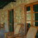 A shaded covered veranda of a rustic stone cottage furnished with wooden lounge chairs and glass doors.