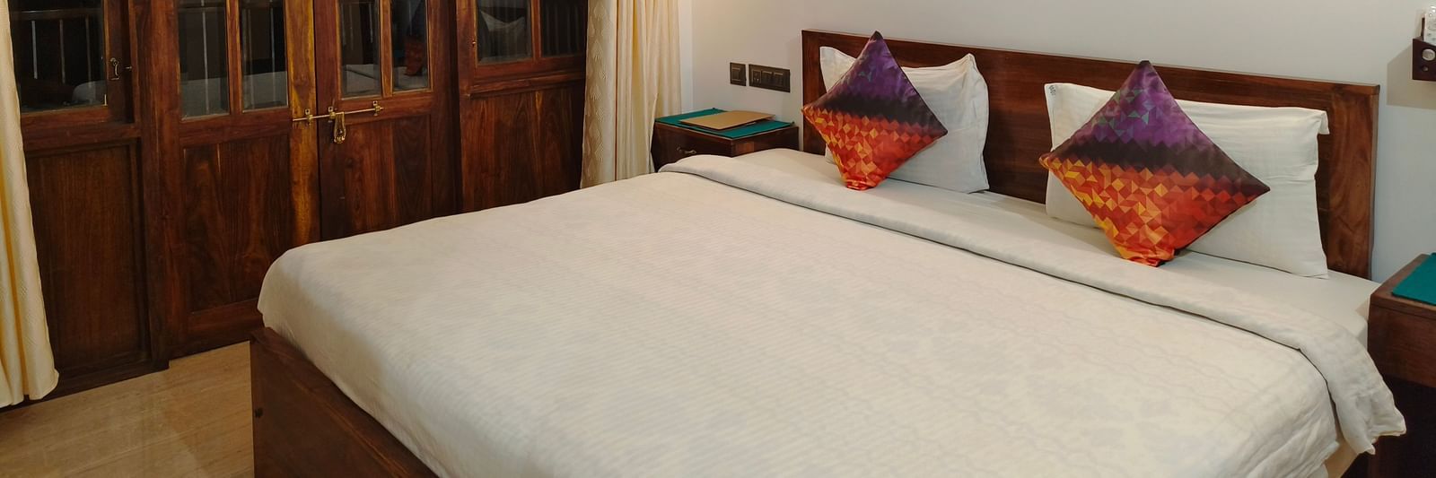A double bed with colourful pillows and a frame hanging on the wall at 103 room at Ananda Holiday Home, Wayanad 4