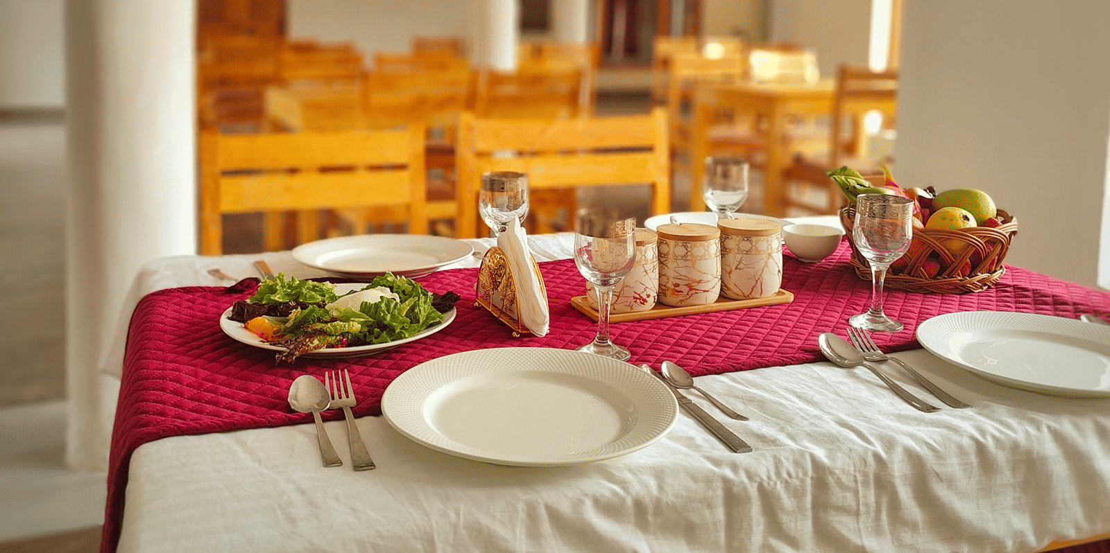 A set dining table with a red runner and white crockery in a bright, airy restaurant at Indus Serenity Retreat.