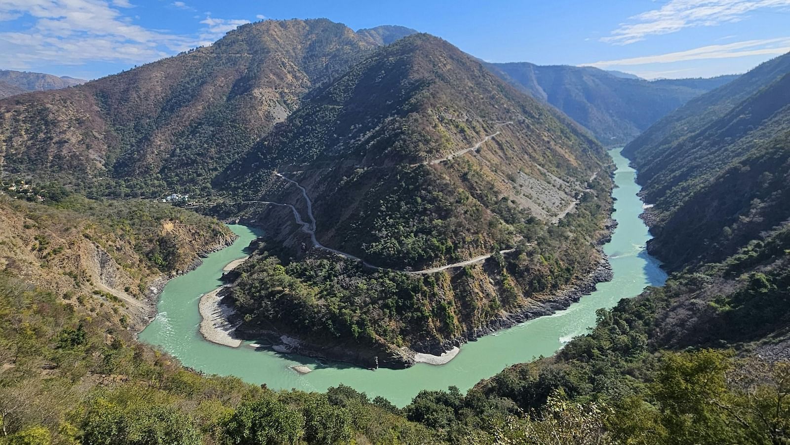 Winding river cutting through lush green hills under a clear blue sky.
