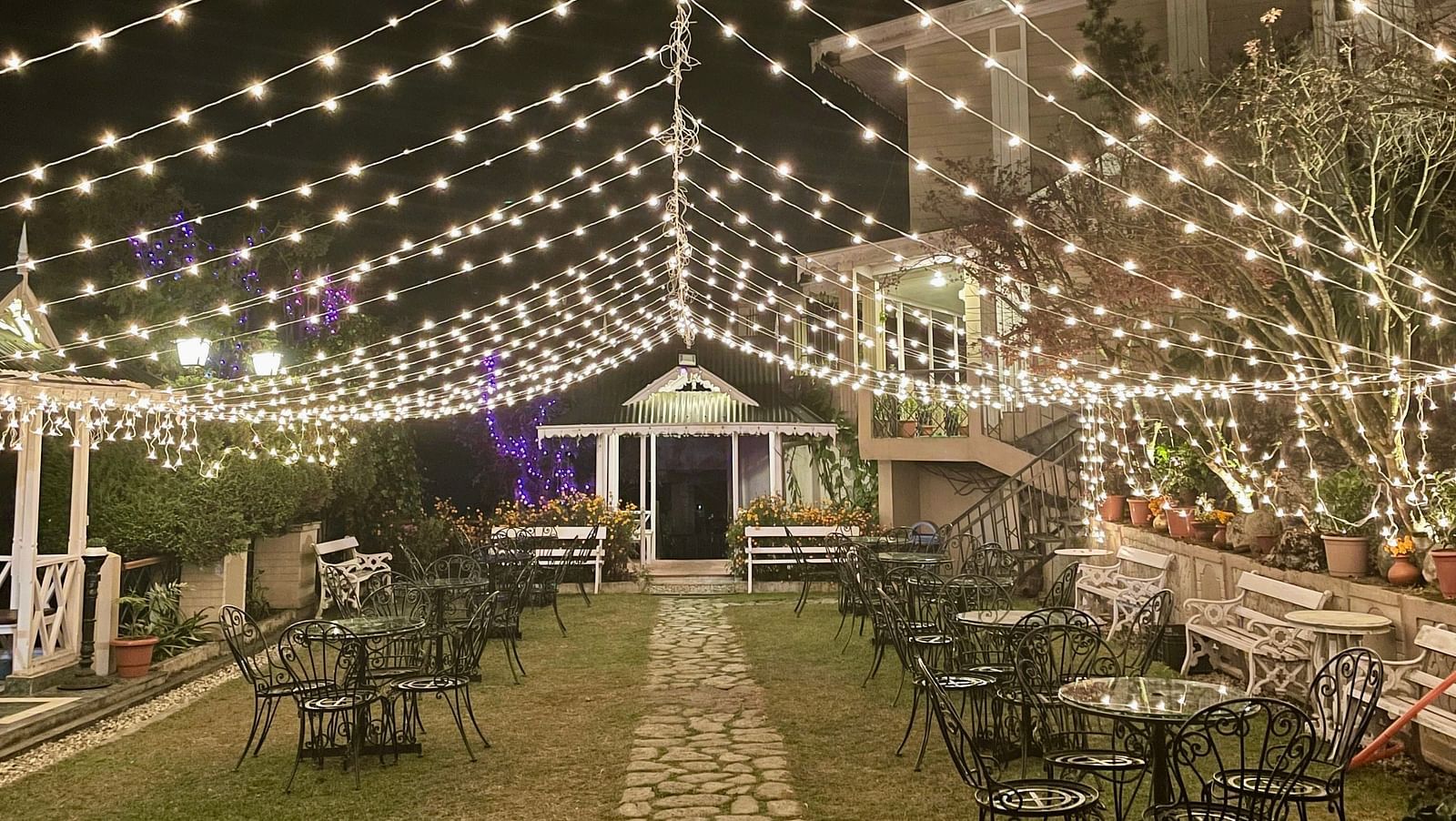 Evening wedding event at Cedar Inn, Darjeeling, showing festoon lights over the garden walkway and decorated seating area.