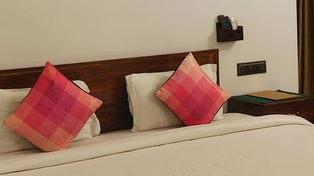 Front view of a double bed with two pink pillows kept on it and hexagonal frames hanging on the wall in 101 non-ac room at Ananda Holiday Home, Wayanad 1
