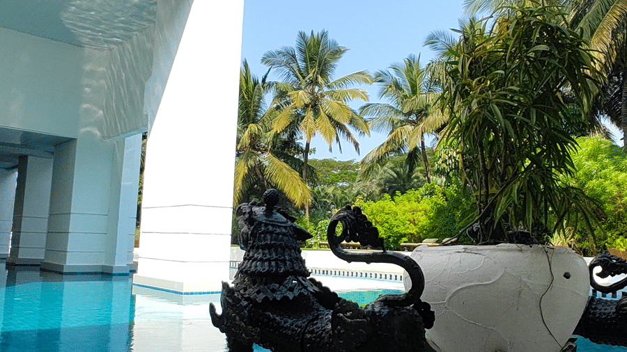 The Mansion House resort outdoor area with swimming pool, decorative black lion statue, cushioned chair, balcony, and palm trees, creating a serene tropical luxury setting.