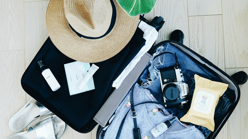 A suitcase filled with travel essentials like a camera, hat and more 