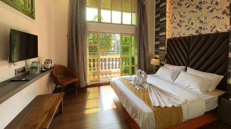 Sunlit premium room featuring a wall-mounted TV, decorative stone wall accents, and luxury bedding - DAN Resorts & Weddings, Palghar
