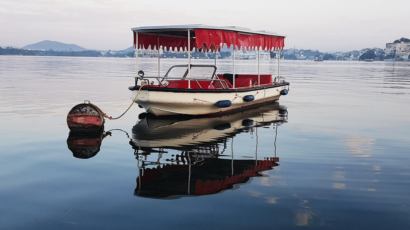 A covered boat anchored on lake with reflections visible on the water, set against distant hills.