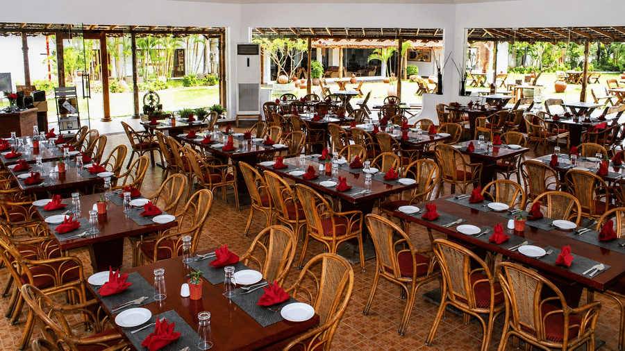 Kapi Multicuisine Restaurant dining hall with wicker chairs and red table settings, offering a bright and airy dining atmosphere