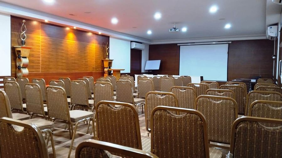 Conference hall with neatly arranged chairs and a projector screen at Hotel Dr Rajkumar International.