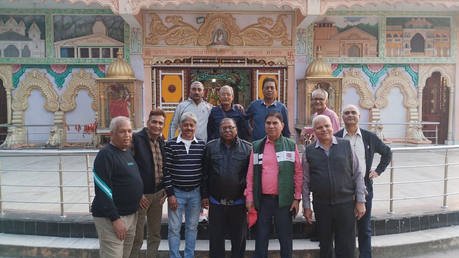 Group of men posing in front of a colourful temple facade with intricate artwork and arched designs.