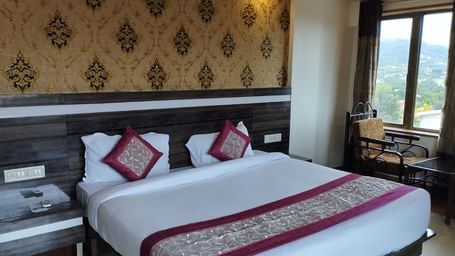 The Super Deluxe Room of Mountview Resort features a king size bed, bedside tables, and a seating area beside the glass windows that offer views of the natural surroundings.