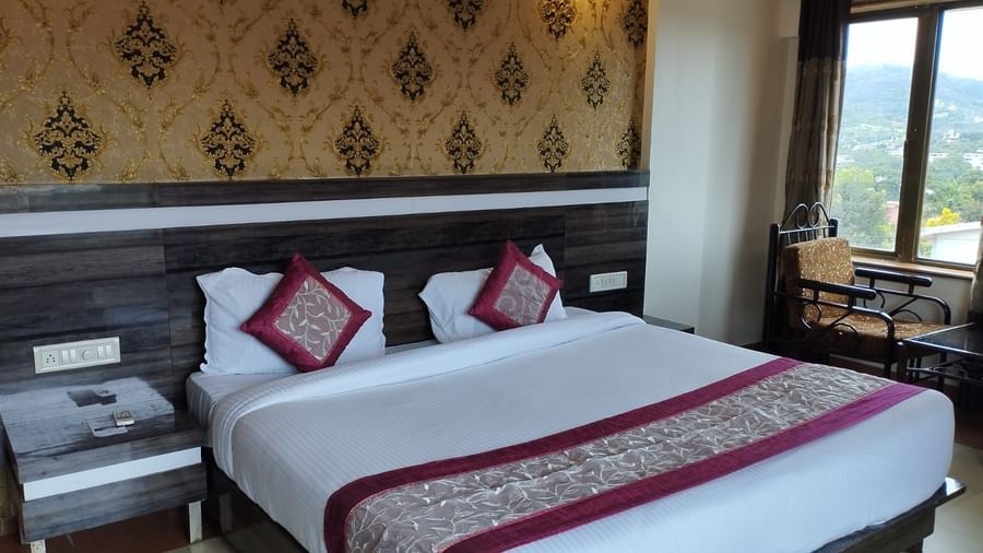 The Super Deluxe Room of Mountview Resort features a king size bed, bedside tables, and a seating area beside the glass windows that offer views of the natural surroundings.