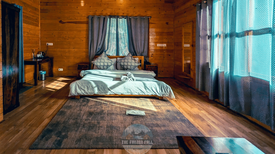 A wood-panelled Deluxe bedroom at Dawat e Drung by FrozenFall Resort, Drung, Tangmarg, with a double bed, window curtains, a large rug and floorboards.
