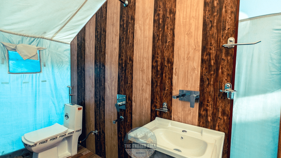 A bathroom at Dawat e Drung by FrozenFall Resort, Drung, Tangmarg, with a toilet, a sink basin and wood-effect wall tiles in a tent structure.