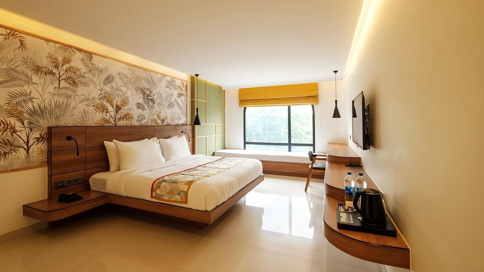 A spacious room at Indie Stays, Jaipur, with a large bed featuring a wooden headboard, a wall-mounted TV with a wooden shelf below, and a large window with an alcove.
