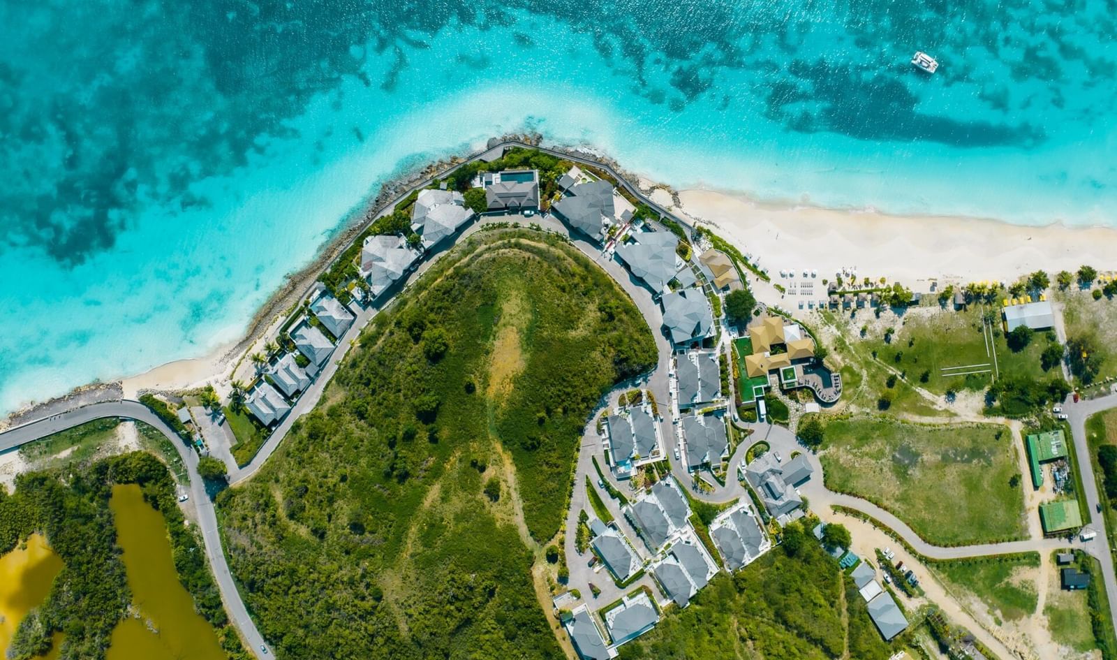 Aerial view of Tamarind Hills Resort in Antigua, nestled between lush greenery and turquoise Caribbean waters along a white-sand beach.