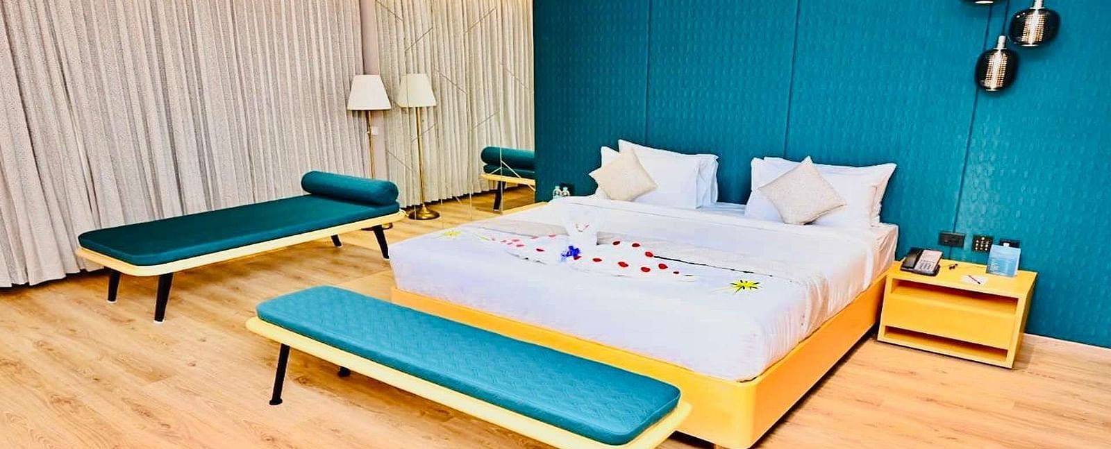 Close up view of a Presedential Suite featuring a King size bed with white linens and decorative swans, a green accent wall, yellow furniture, and hardwood floors - Dhanalakshmi Srinivasan Hotels, Perambalur