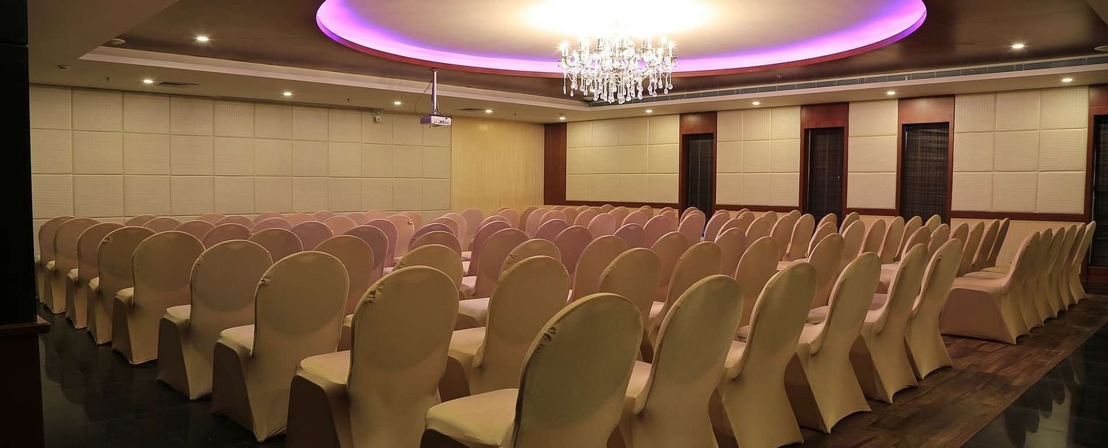 Side view of Orchid Hall at Dhanalakshmi Srinivasan Hotels, Perambalur with  chairs arranged in theatre seating and chandelier on top. 
