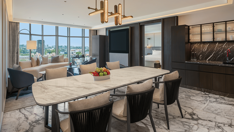 Suite living and dining room with a marble dining table for six, sofa, TV, bar counter and floor-to-ceiling windows over the city at The Residency Towers Chennai.