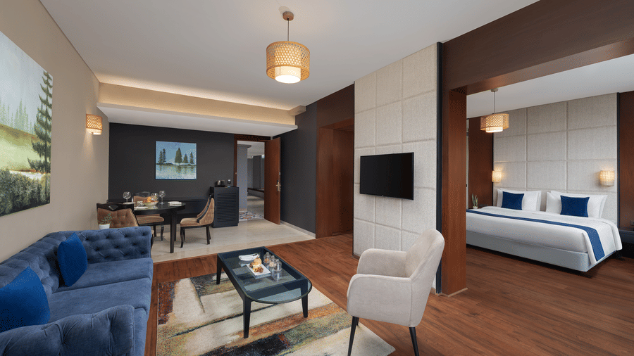 An overview of the living area of the Executive Suite at Essentia Luxury Hotel, Indore with sofa seating and coffee table set up and the bedroom on the left hand side.