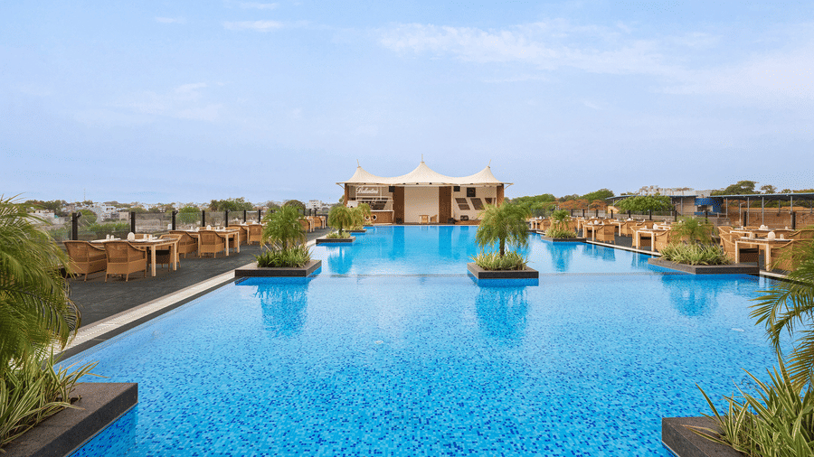 Outdoor swimming pool at Essentia Luxury Hotel, Indore, featuring crystal clear water surrounded by greenery under a blue sky