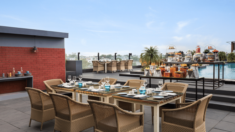 Rooftop seating arrangement at one of the best restaurants in Indore at Essentia Luxury Hotel, featuring a pool under a clear sky