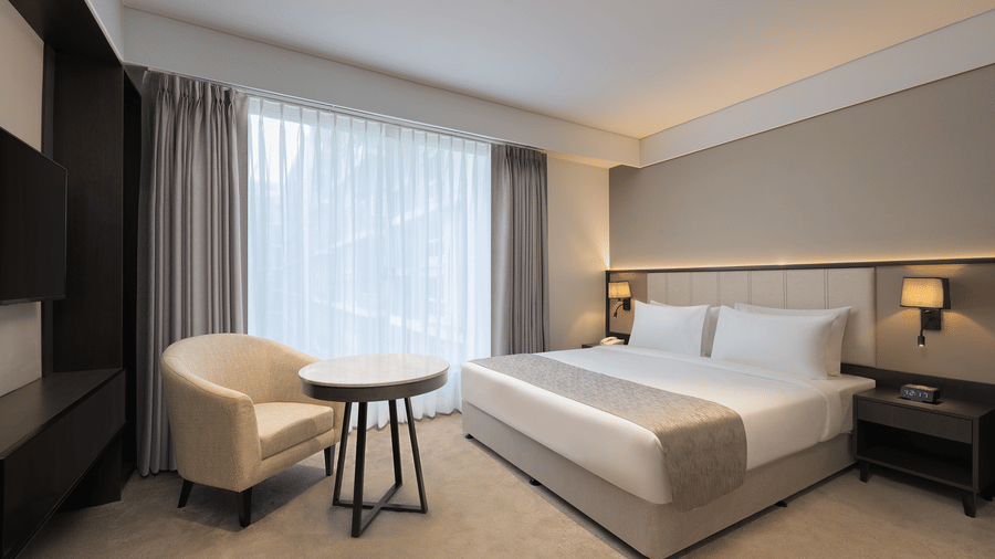 Deluxe King Room with a king size bed and a comfortable chair beside a large window with curtains on at Essentia Premier offering the best stay in Pune