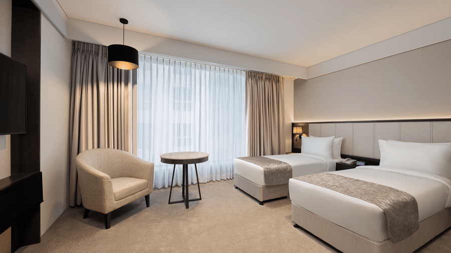 One of the Deluxe Twin Rooms in Pune featuring twin beds by the window and a seating area next to the wall at Essentia Premiere, Pune