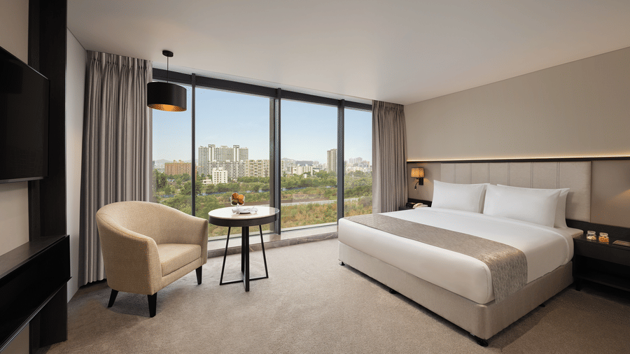 An overview of Premier Room with a king size bed and a sofa beside a large window at Essentia Premiere, Pune.