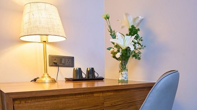 A corner of a room with a lamp and a flower vase placed on a table and a chair infront of it for comfortable seating