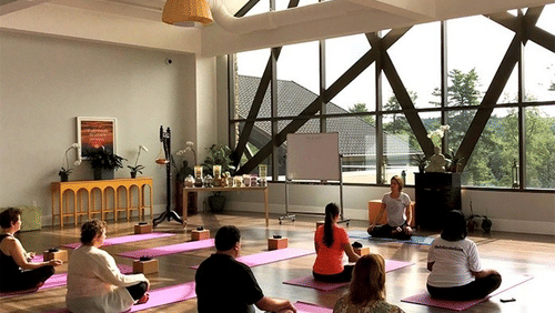 A group of people sitting in a circle at YO1 Longevity & Health Resorts on yoga mats in a sunlit studio with large windows.