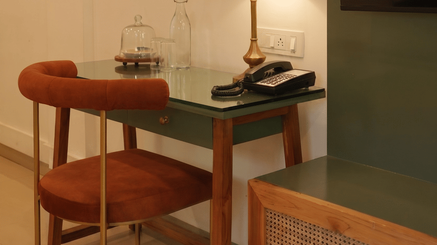 A wooden desk with a lamp, a chair, and a mounted television screen at Oceanature Resort, Alibaug.