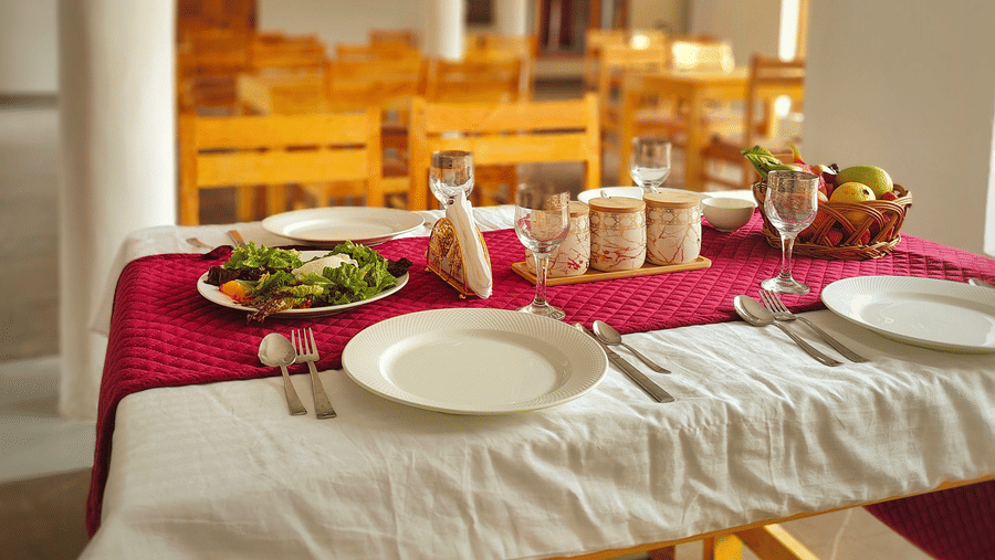 A set dining table with a red runner and white crockery in a bright, airy restaurant at Indus Serenity Retreat.
