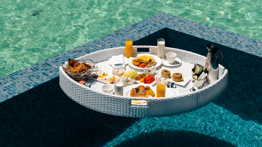 a floating breakfast tray floating on an infinity swimming pool with the ocean in the background