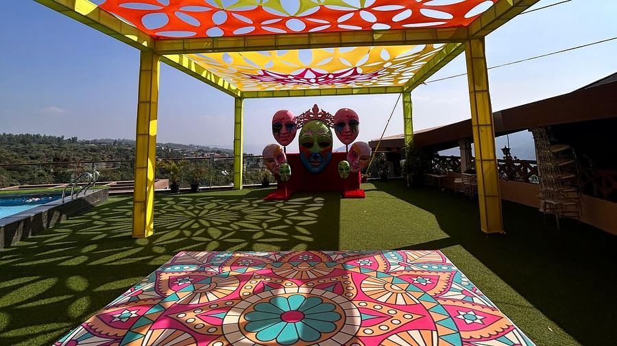 A lawn decorated in Carnival theme featuring a mandala designs made on the ground, cut out fabric designs on top supported by four pillars and a stage where several masks are hanged - The Grand Legacy Resort & Spa 
