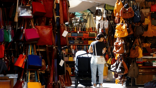 A close up of the many hand bags hung on the side of a street shop to be sold.