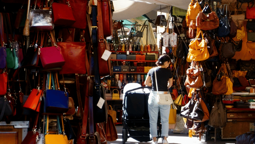 A close up of the many hand bags hung on the side of a street shop to be sold.