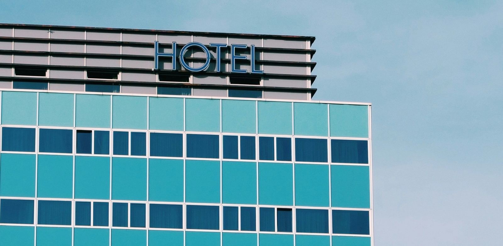Close-up of the top of a modern high-rise office building with blue glass windows, featuring signage with the text in white letters against a turquoise sky.