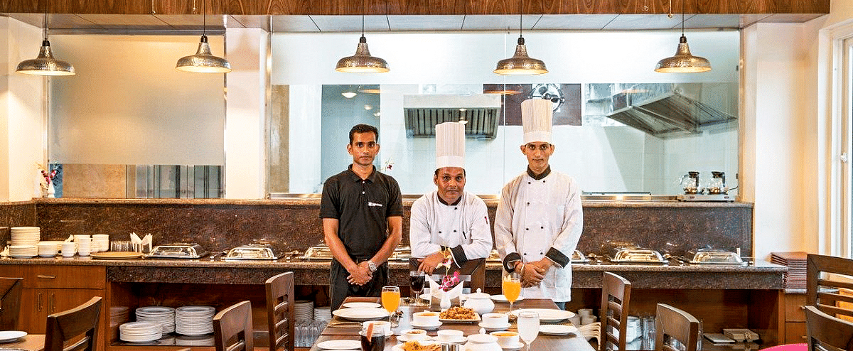 Three staff members of Regenta Inn DLS standing in front of a long dining table featuring a wide spread of delicious dishes.